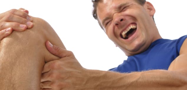 Male athlete on floor clutching knee and hamstring in excrutiating pain on white background D90 #3369140